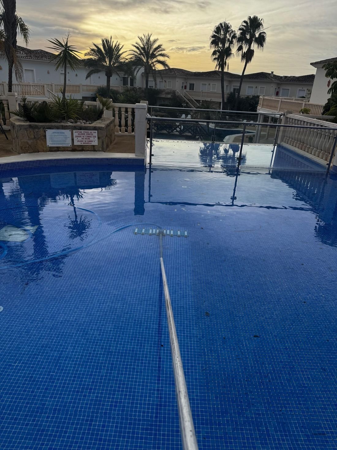 Limpieza del vaso de una piscina de urbanización al atardecer con recogehojas