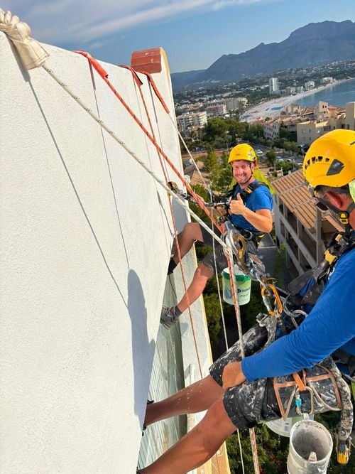 Dos operarios pintando la fachada de un edificio con vistas a la bahía
